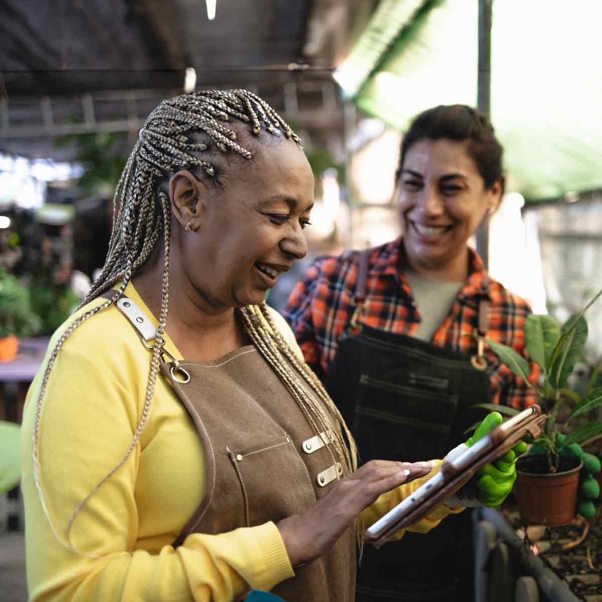 Two women wearing work aprons in a greenhouse