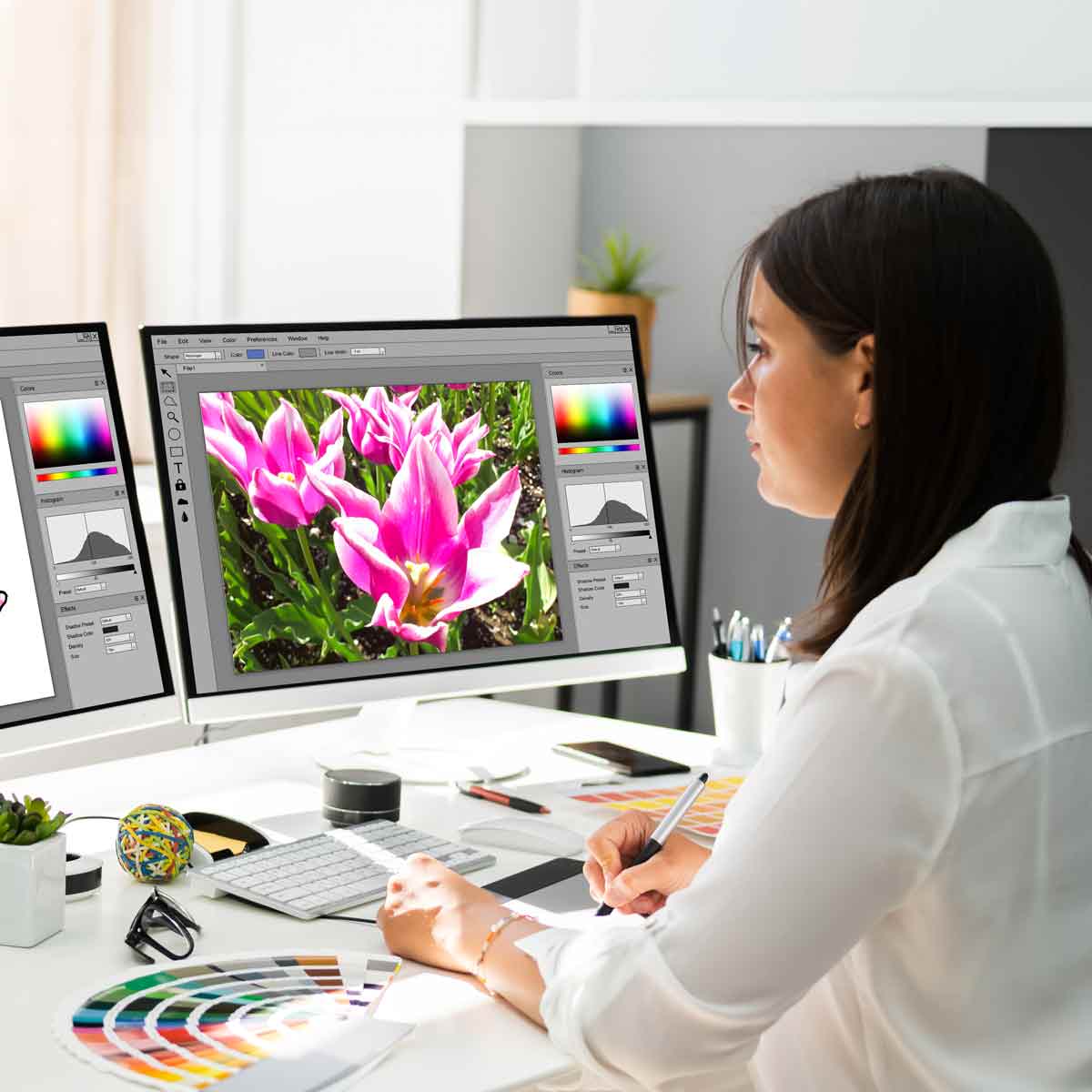 A graphic designer creating an image of a flower, using two computer screens and Pantone swatches