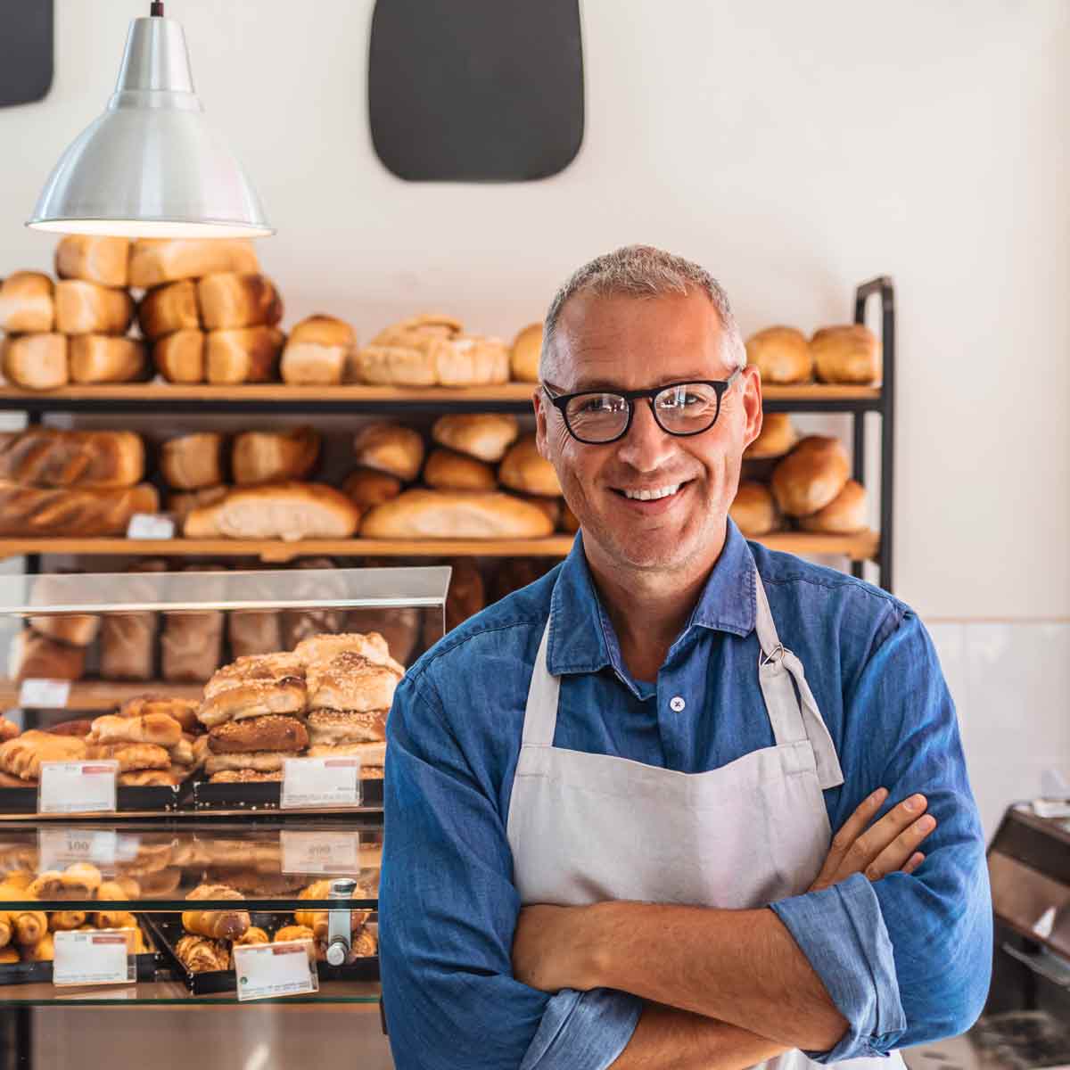 A cheerful man in an apron standing outside a bakery, ready to welcome customers