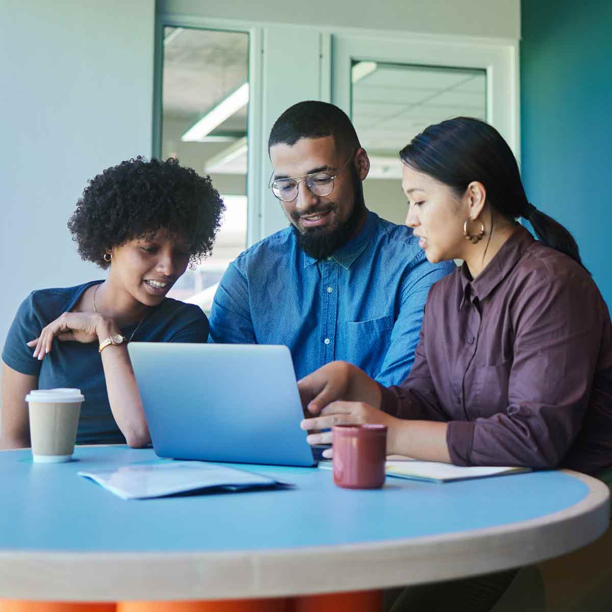 Group of three people sitting at a table engaged in a discussion while using a computer