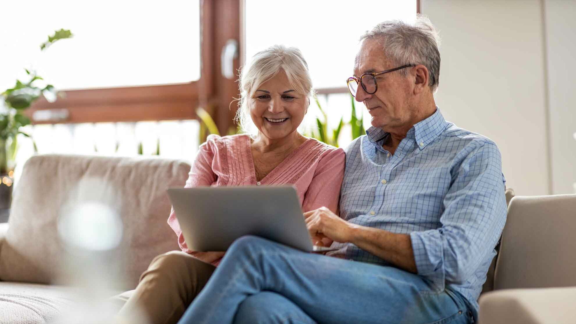 Senior man and woman relaxing on a sofa, using a laptop computer.