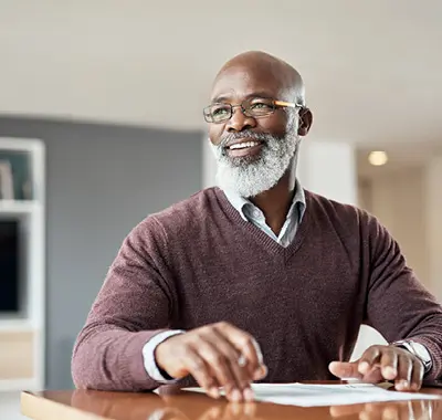 A bearded senior man wearing glasses sitting at a table, engrossed in his work.