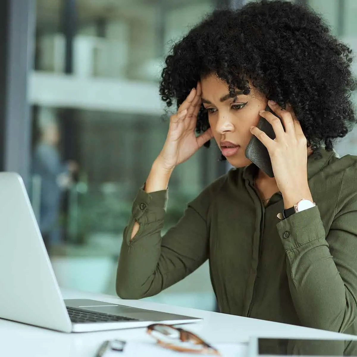 Upset African-American woman sitting at a desk with a laptop and cell phone.