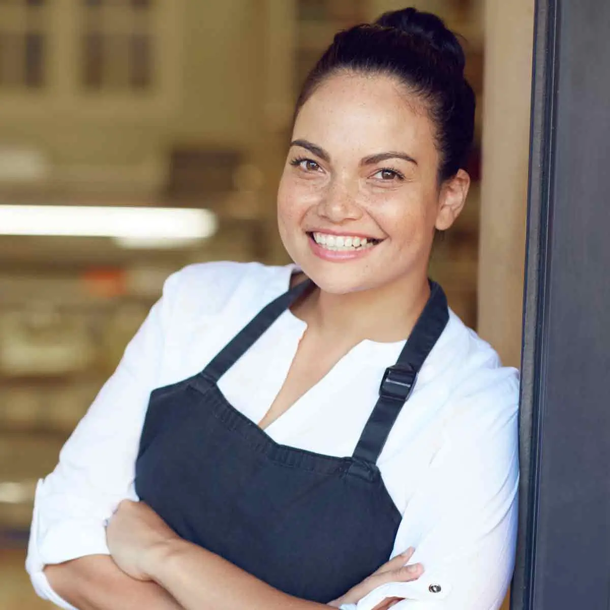 A woman wearing an apron smiles warmly at the camera, radiating a sense of joy and friendliness.