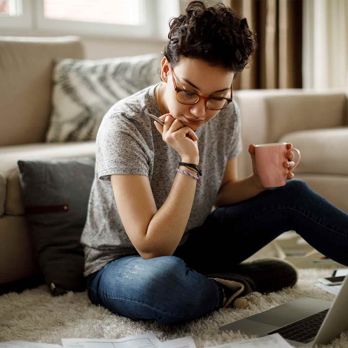 A woman sitting on the floor with a laptop and coffee.