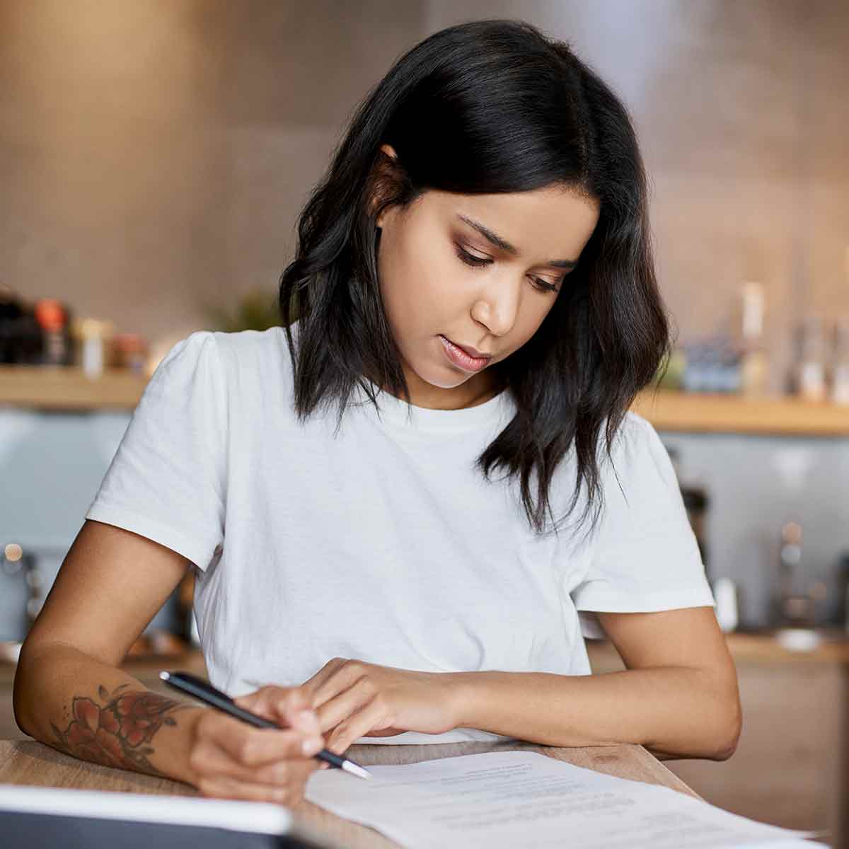 A lady sitting at a table, writing on a piece of paper.