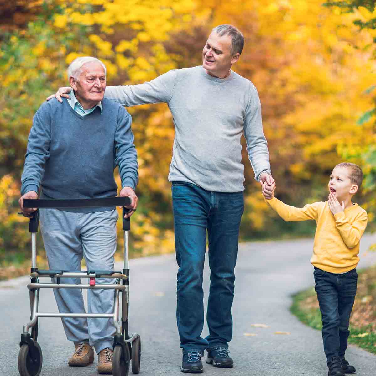 Grandfather, son, and grandson taking a walk, the older man supported by a walker.