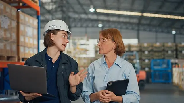 Female manager wearing a safety helmet has a discussion with a female professional in a warehouse