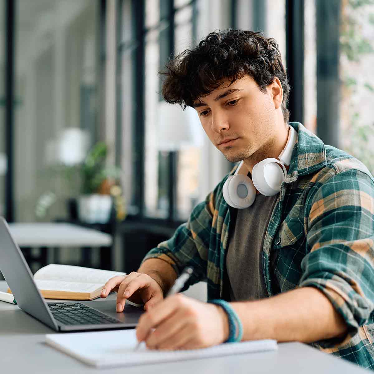 A male college student wearing headphones works on a laptop.