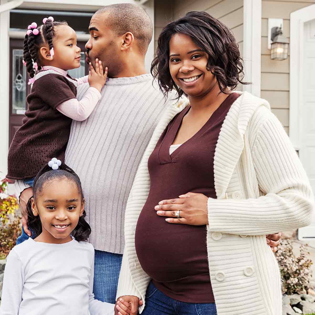 A pregnant woman and her family stand in front of their home, a heartfelt moment of excitement for the future.