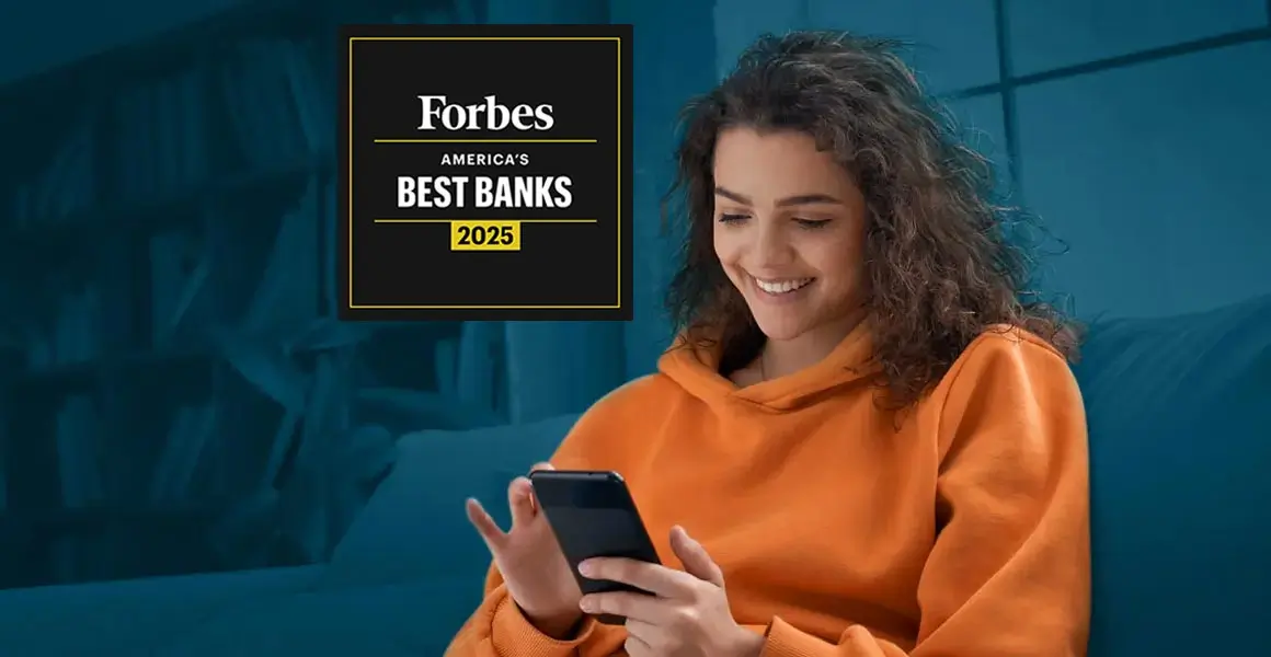 The image depicts a person in an orange hoodie sitting on a blue couch, looking at a smartphone. The individual’s face is pixelated for privacy. In the foreground, there’s a red and black banner with the text “AMERICA’S BEST BANKS Forbes 2025.” The room appears dimly lit with blue ambient lighting.