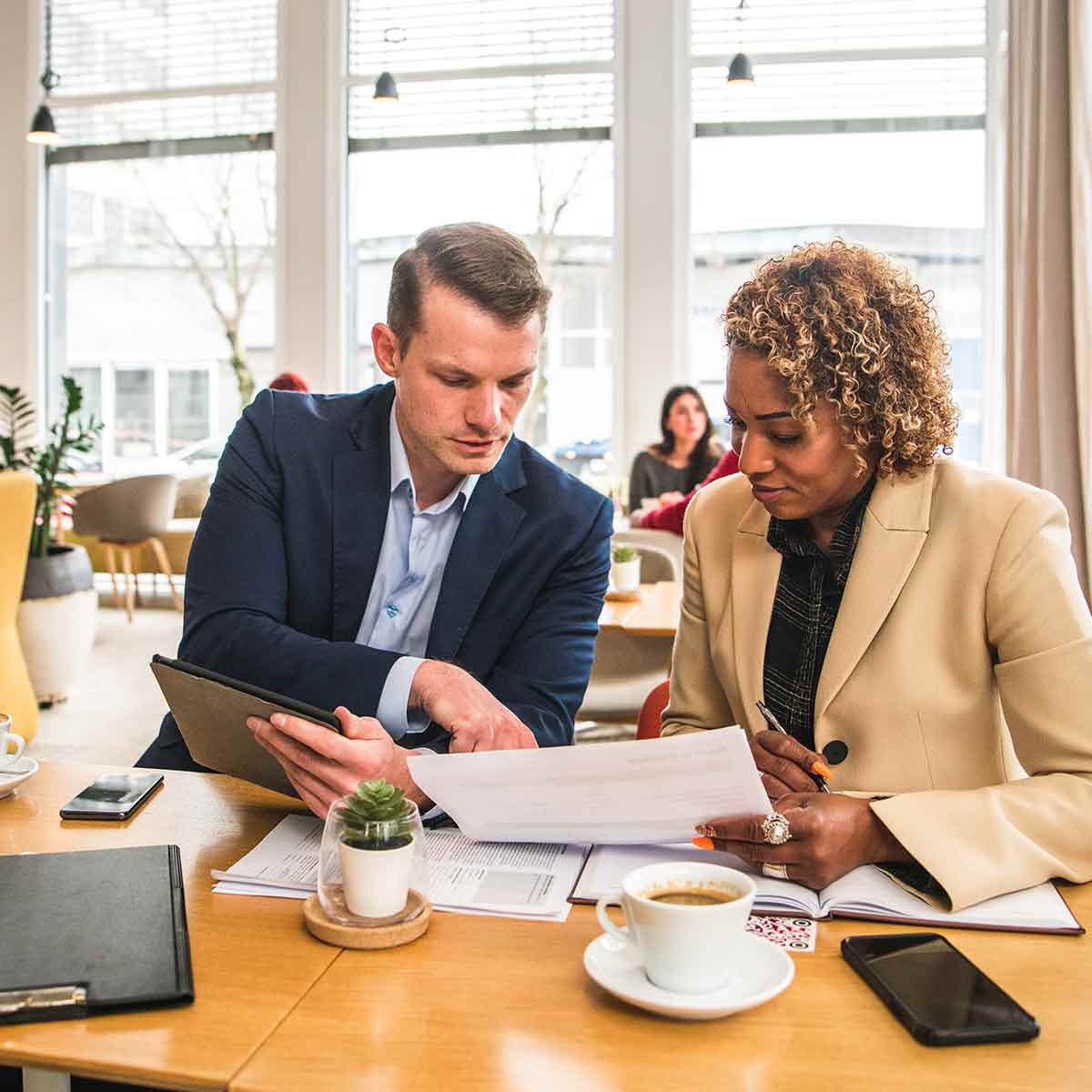 Client and financial advisor looking at documents and talking over coffee, personalizing wealth management strategies