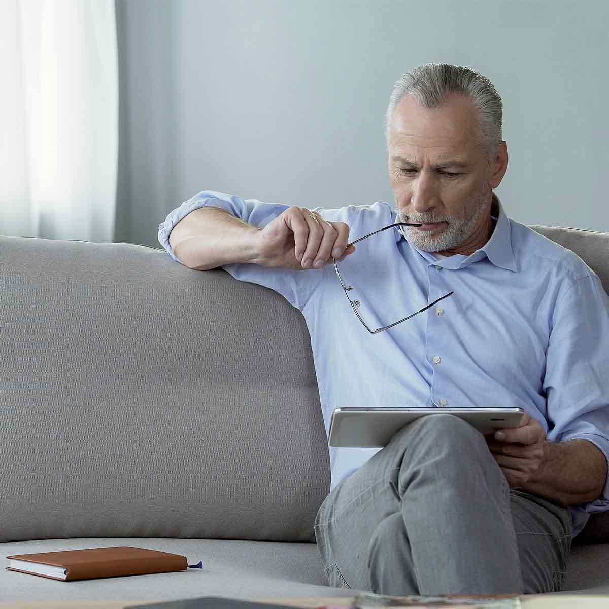 Older man sitting on his couch and reading on his tablet, enjoying an early retirement