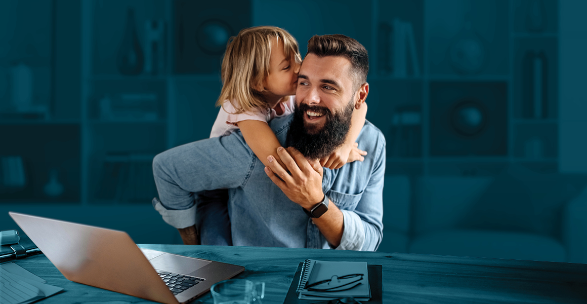 A man and a child are seated at a desk, looking at a laptop screen and playing together