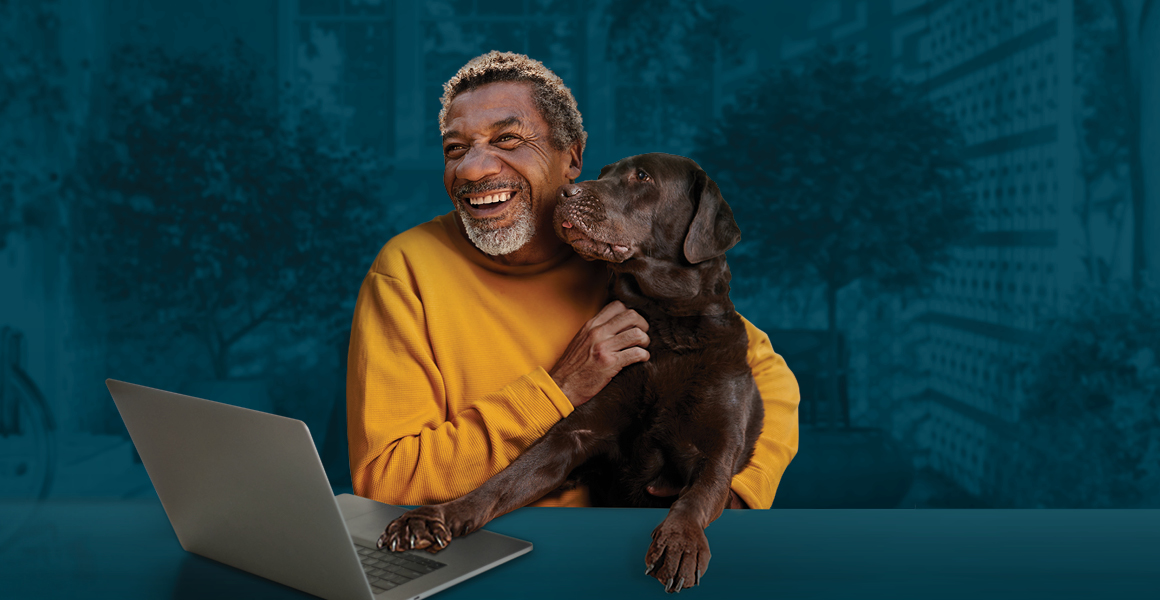 An older man cuddles with his dog in front of a laptop