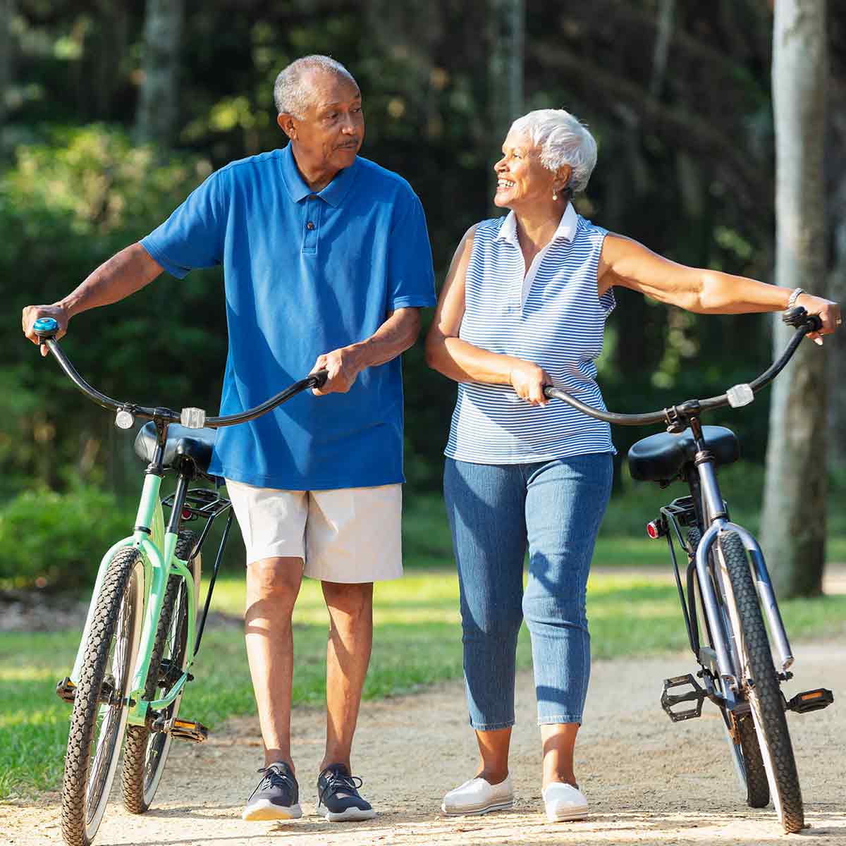 Older couple riding bikes through the woods on a sunny day, enjoying a financially secure retirement.