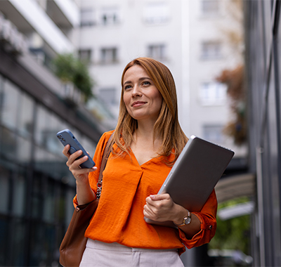 Busy young womanholding smart phone and carrying a laptop