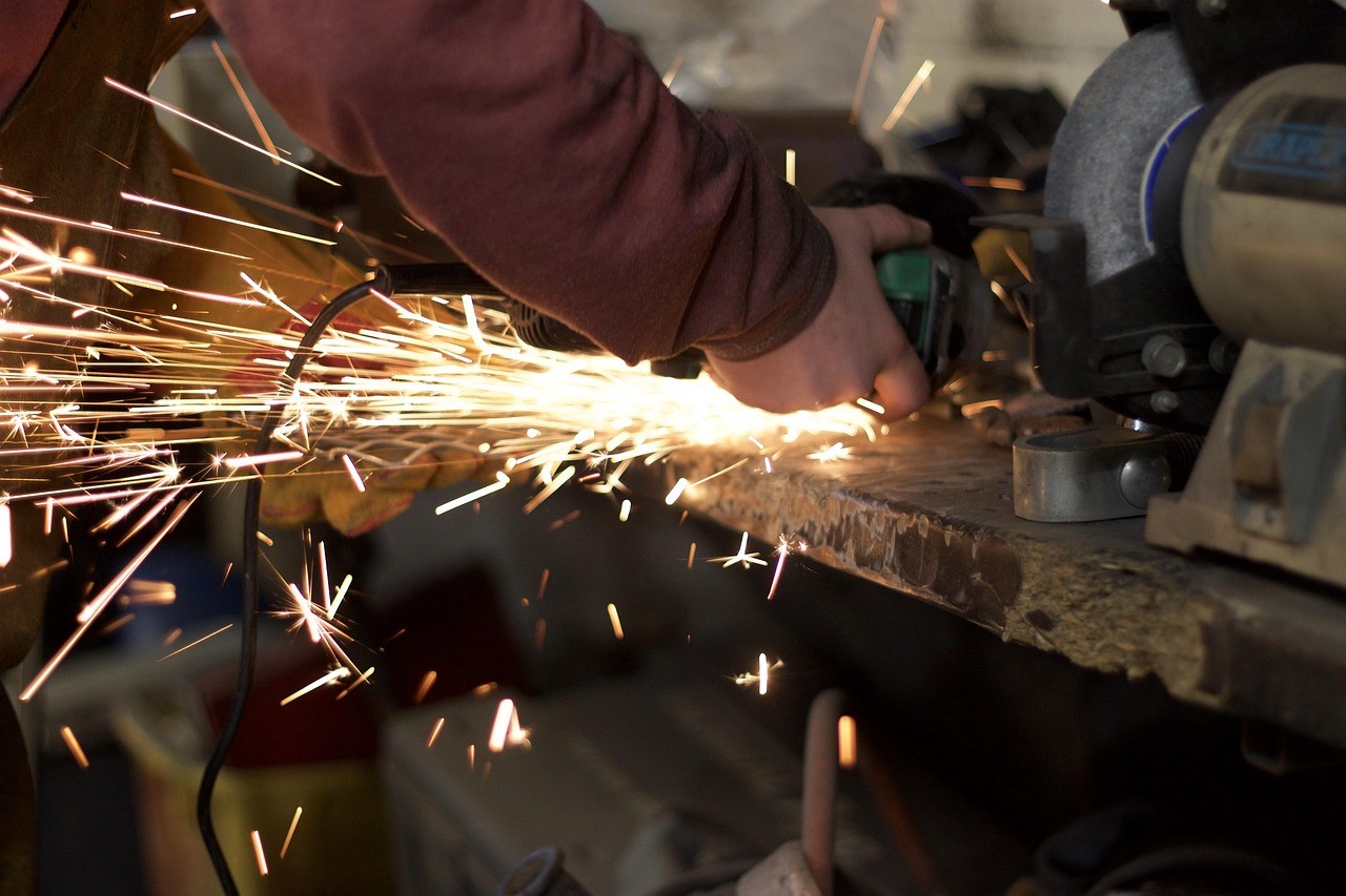 A worker operates a metal grinder, creating sparks as they shape the material.