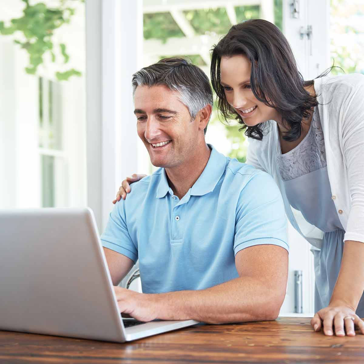 An optimistic couple reviewing their finances on a laptop in the comfort of their sunny kitchen