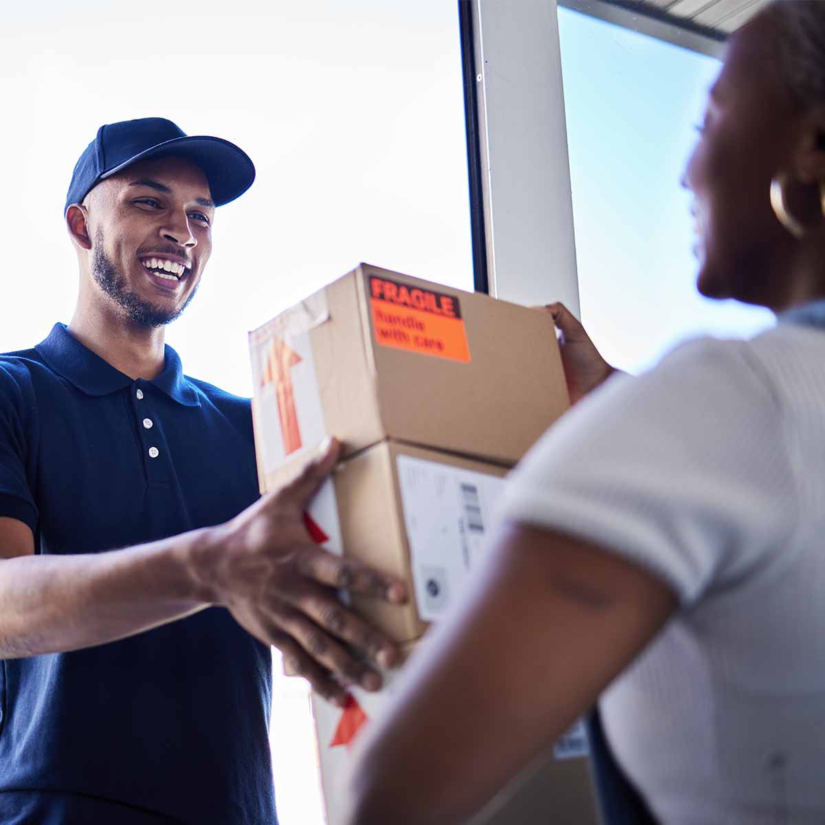 A delivery driver handing a package to a smiling woman on her porch, highlighting the increase of online shopping compared to local retail