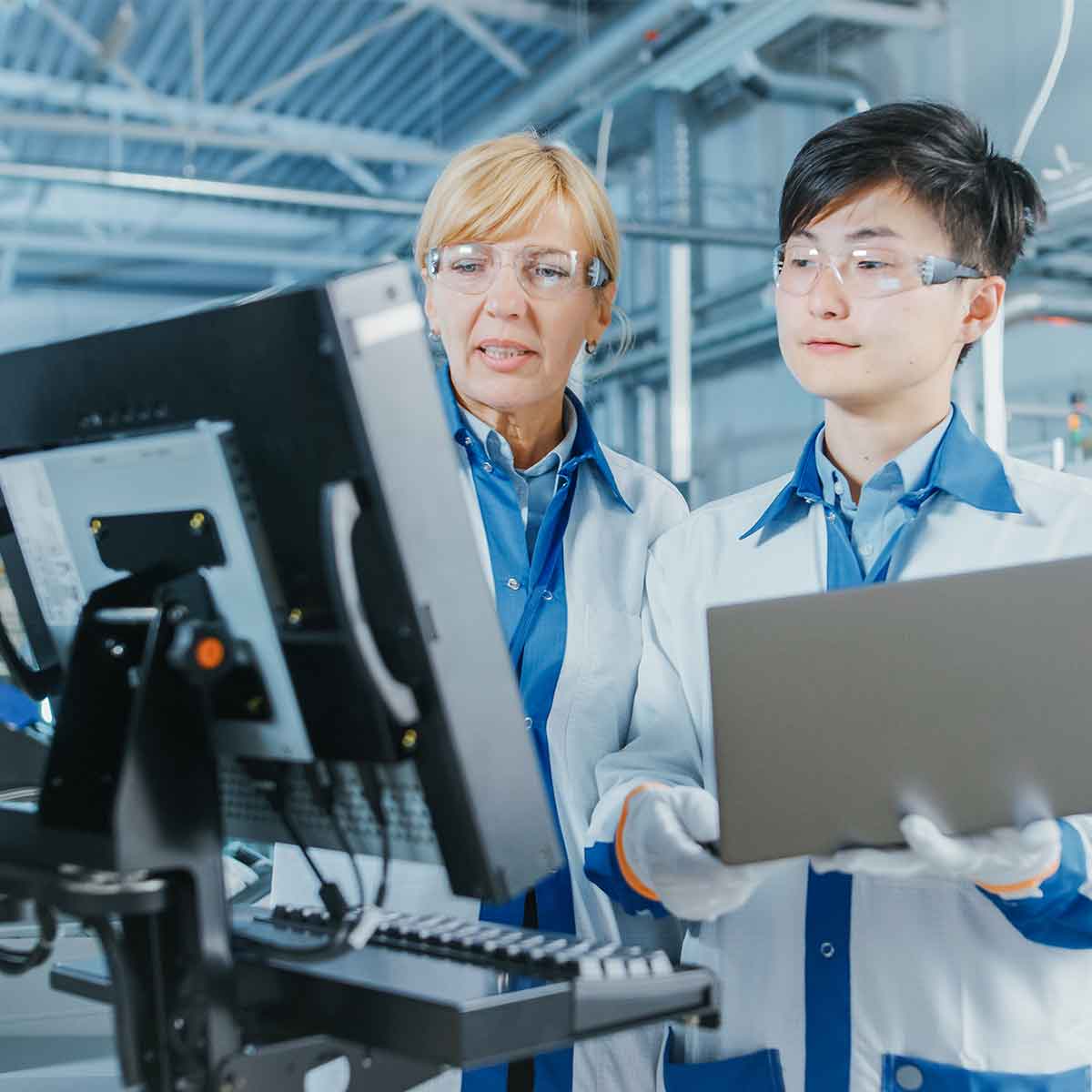 Two medical manufacturing plant workers reviewing data on a computer in cleanroom environment