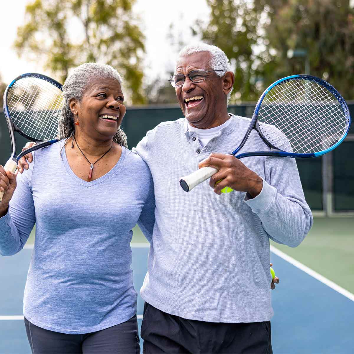 Senior couple laughing on the tennis court, showing how smart strategies can lead to a winning retirement.
