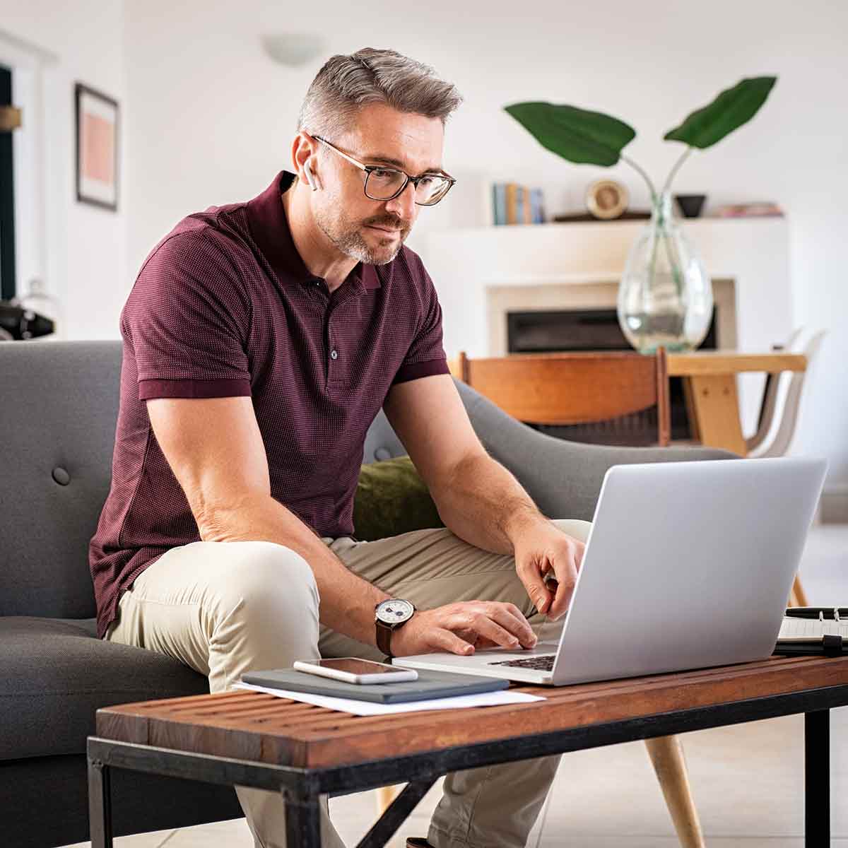 A man working on his laptop in his living room. He looks concerned or focused on something