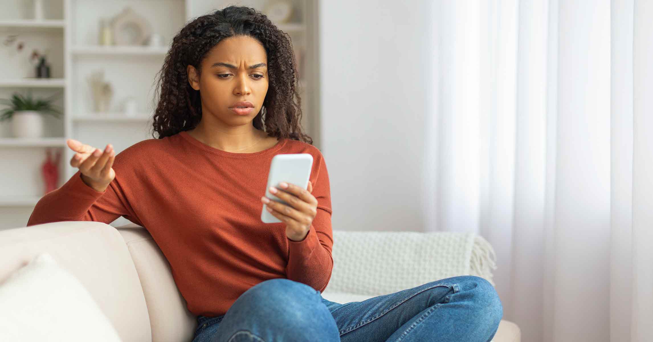 A young woman looking at her phone with a worried expression due to a possible bank scam