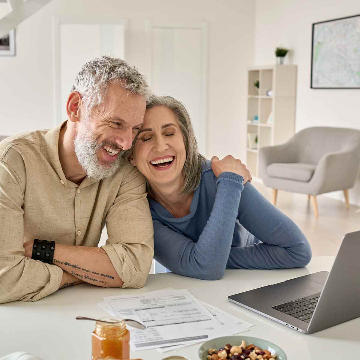 Smiling senior couple using laptop with bills and banking papers on table