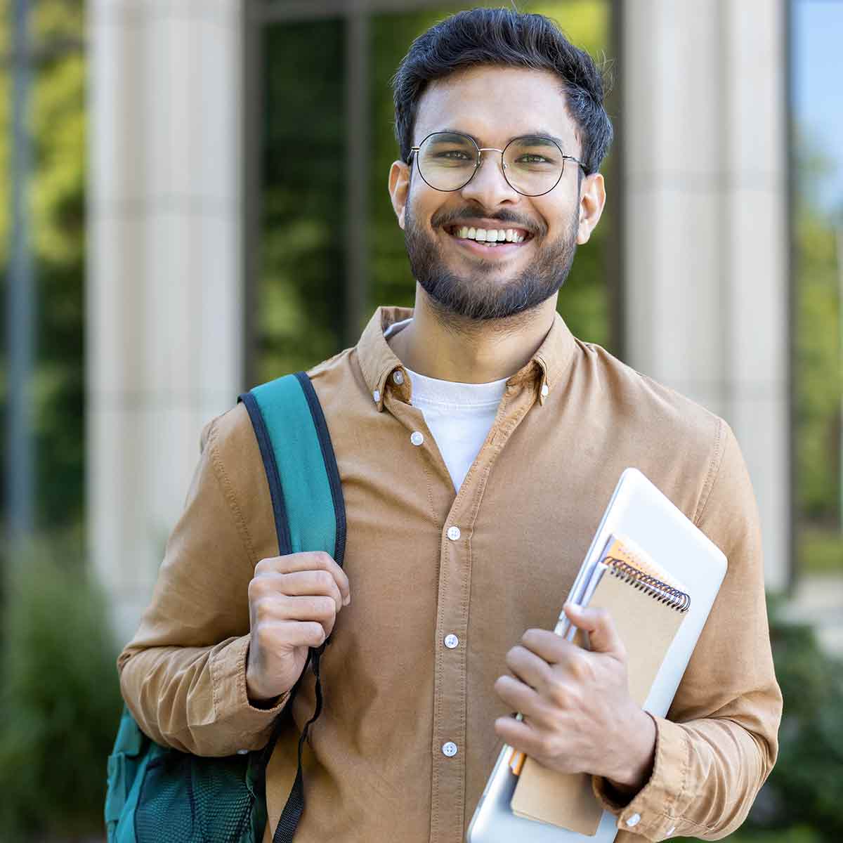 A smiling college student wearing a backpack and holding a notebook