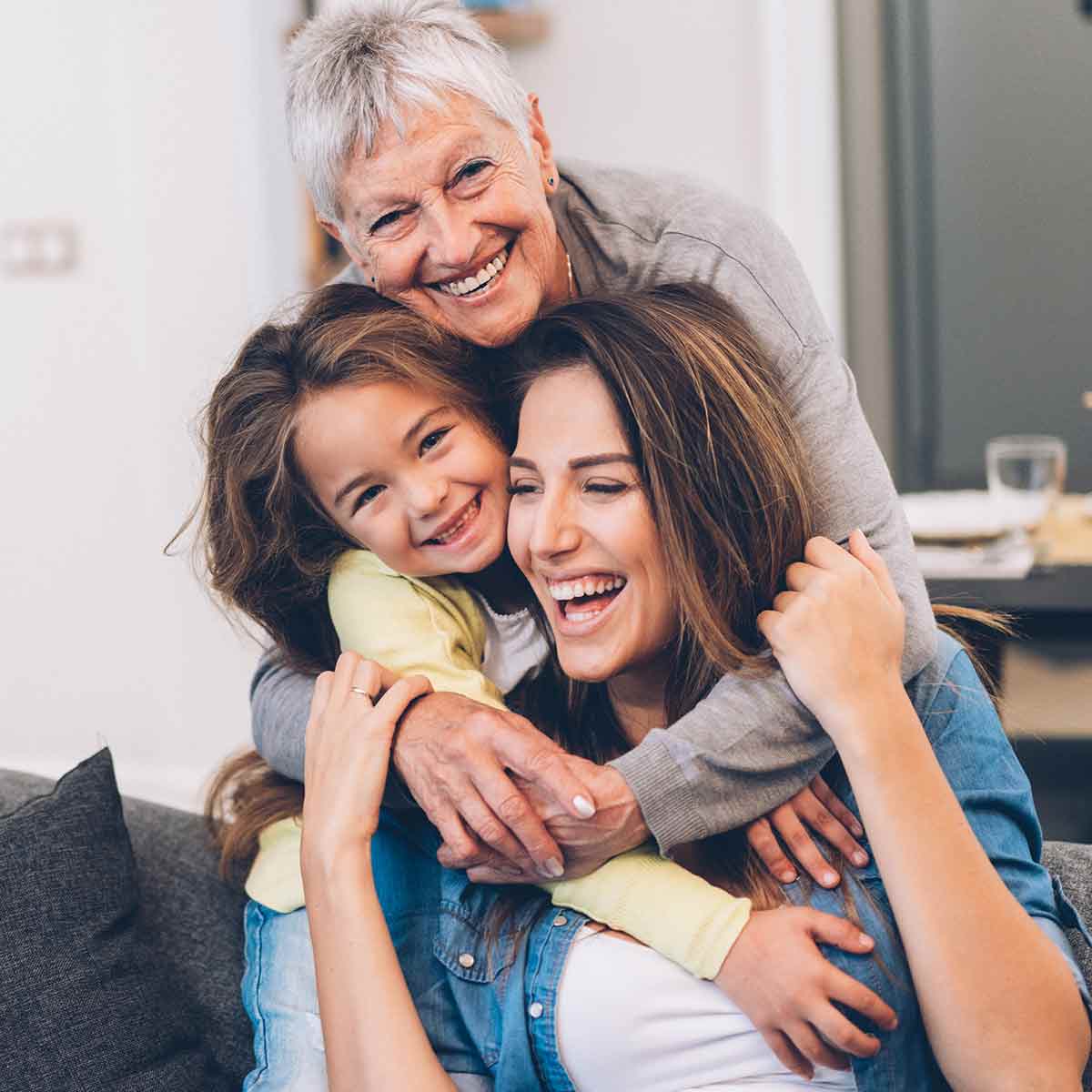 Grandmother, mother, and daughter laughing and hugging on the couch