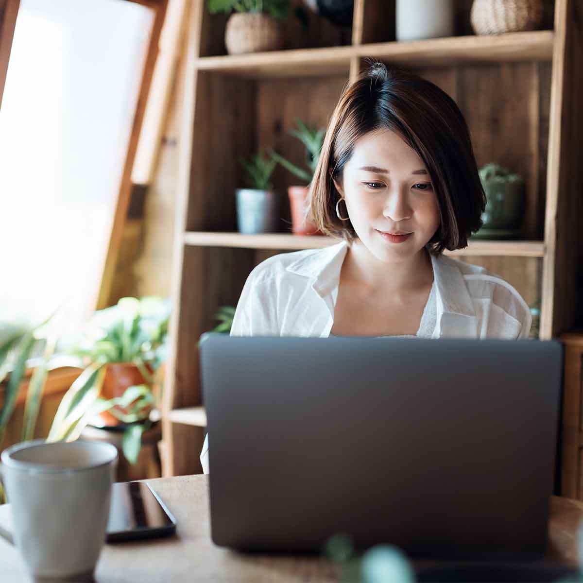 A young woman in her home office, working on her laptop and sipping coffee