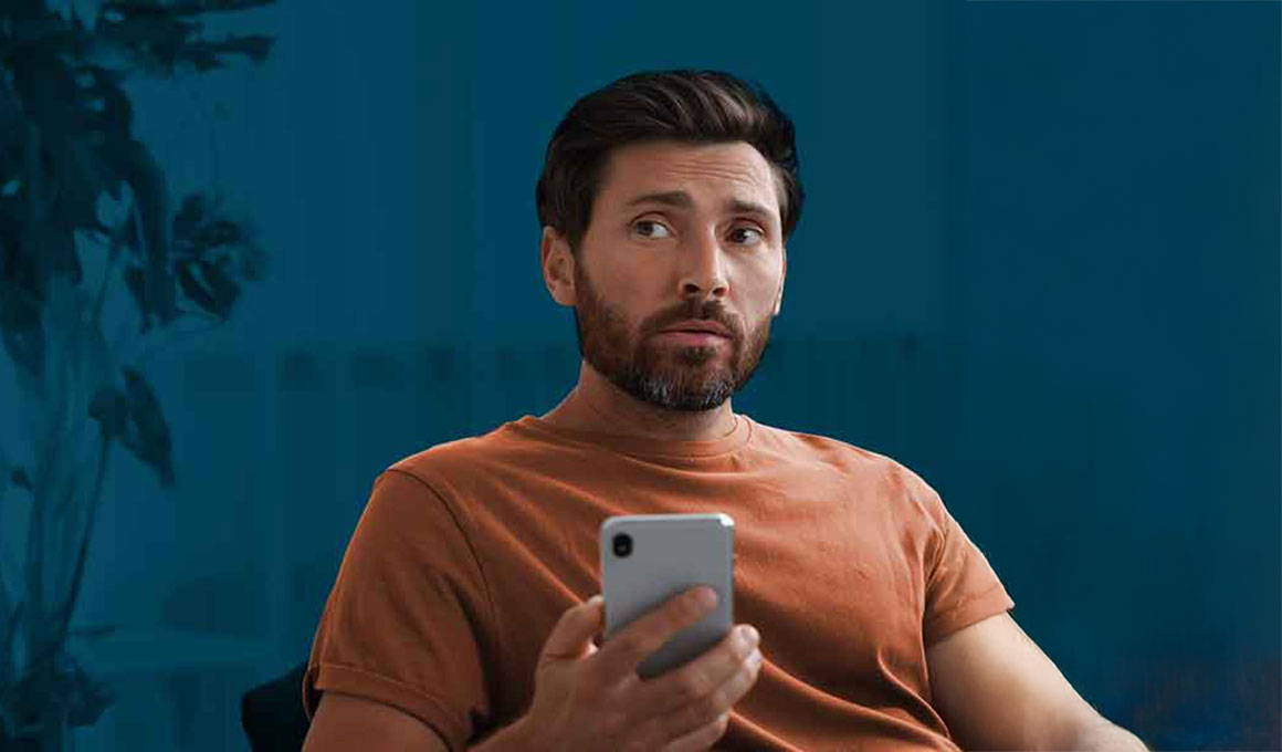 A man suspiciously looks at his phone, determining if the message he received is a banking scam