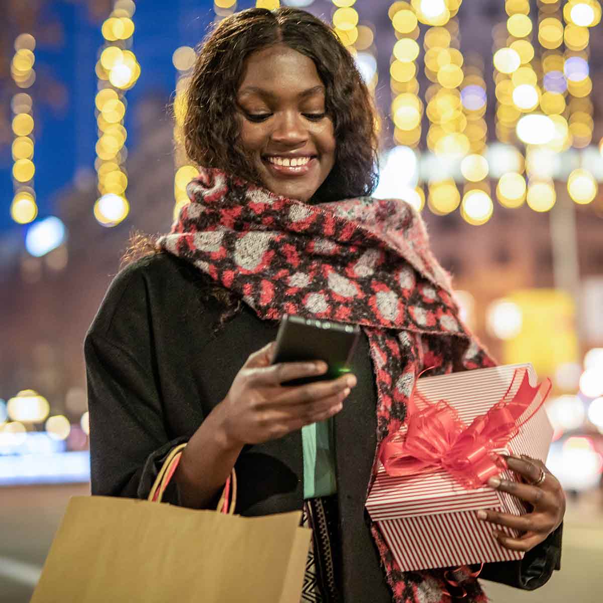 Woman walking down a wintery street carrying shopping bags and giftwrapped presents, using the 1st Source mobile app to manage holiday spending