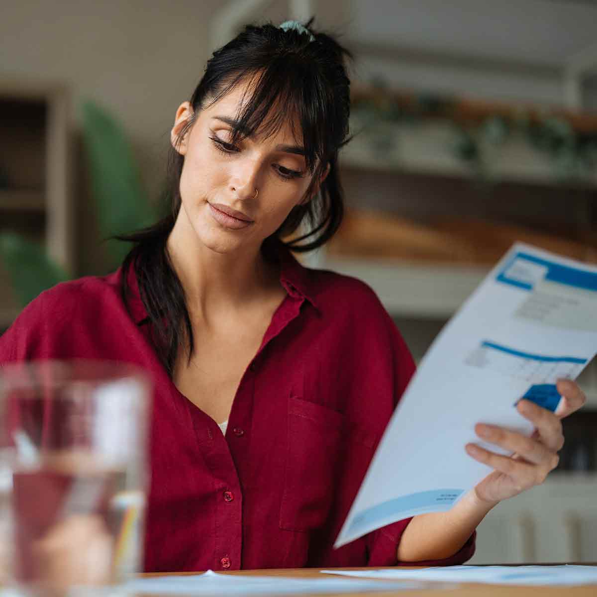 Young woman reviewing a financial document at her kitchen table and writing notes