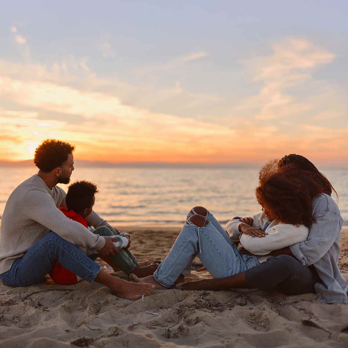 Family sitting on the beach watching the sunset together.