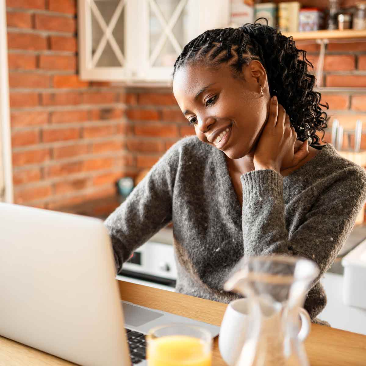 A woman sitting near a window with a laptop, taking a moment to relax with a cup of tea before reviewing her bank account.