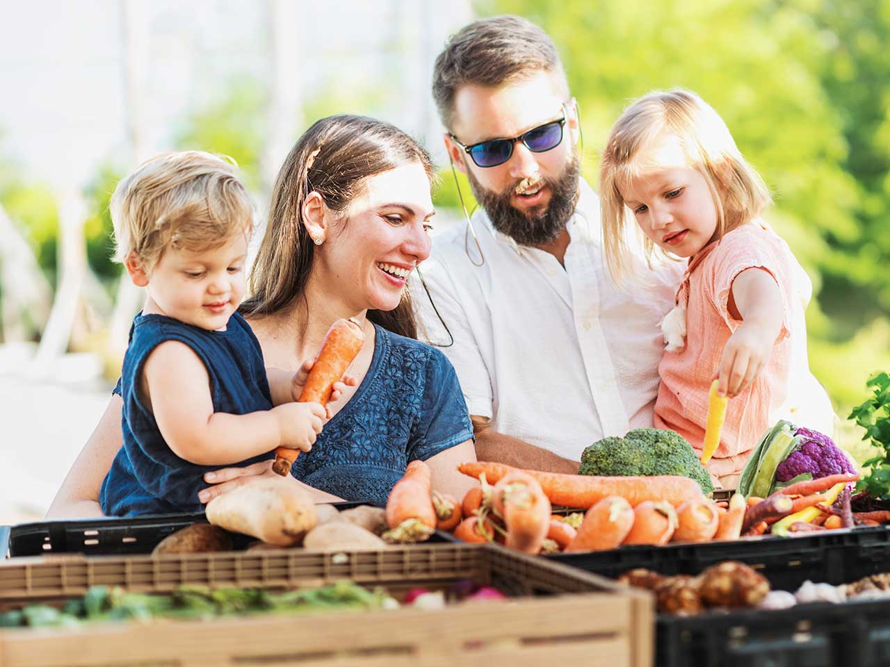 Family of four choosing fresh vegetables at a farmers market.