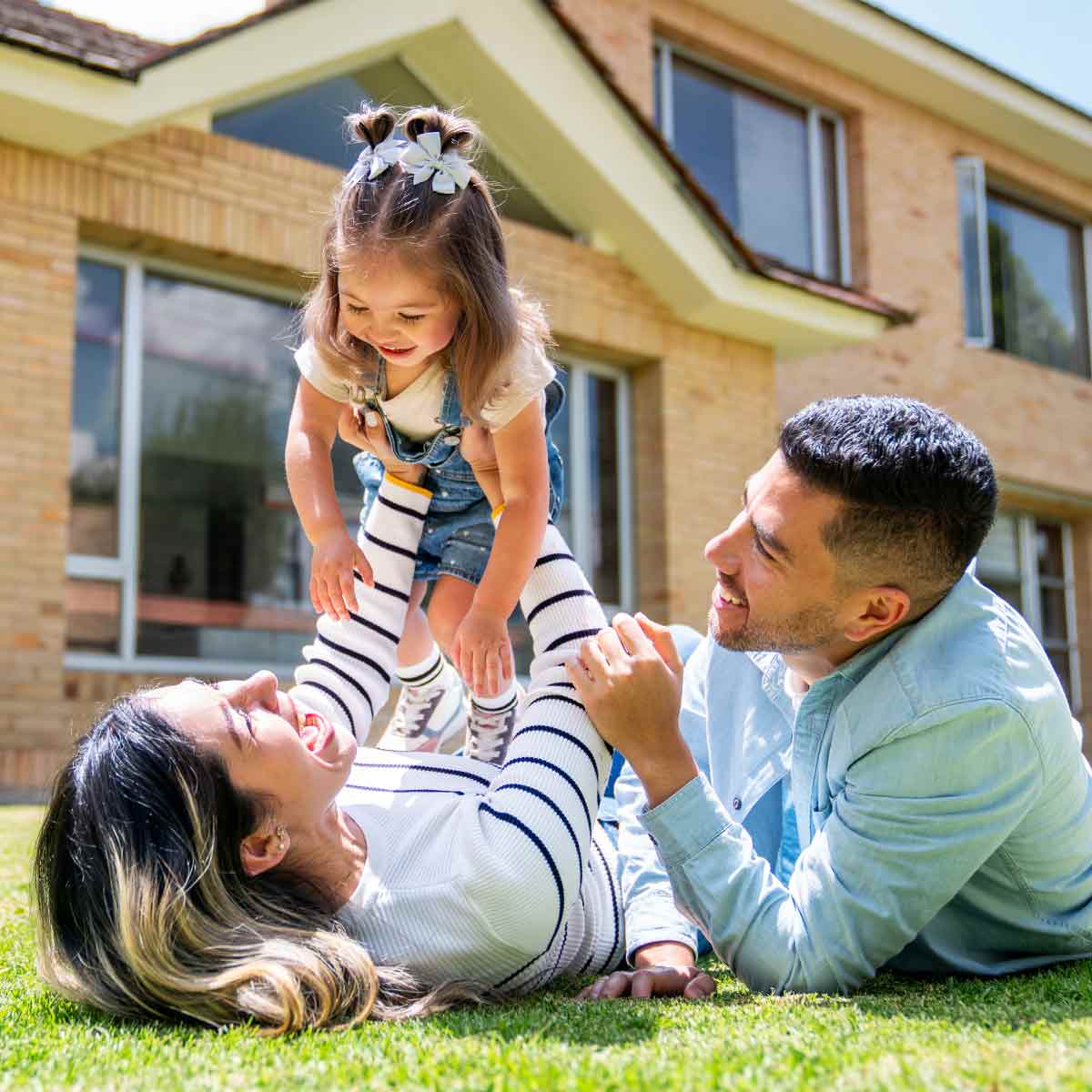 Parents playing with their toddler on the lawn in front of their home