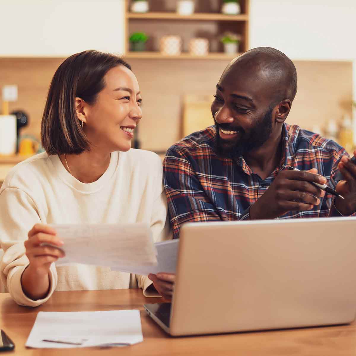 Couple reviewing their finances on a laptop with paper statements at the kitchen table