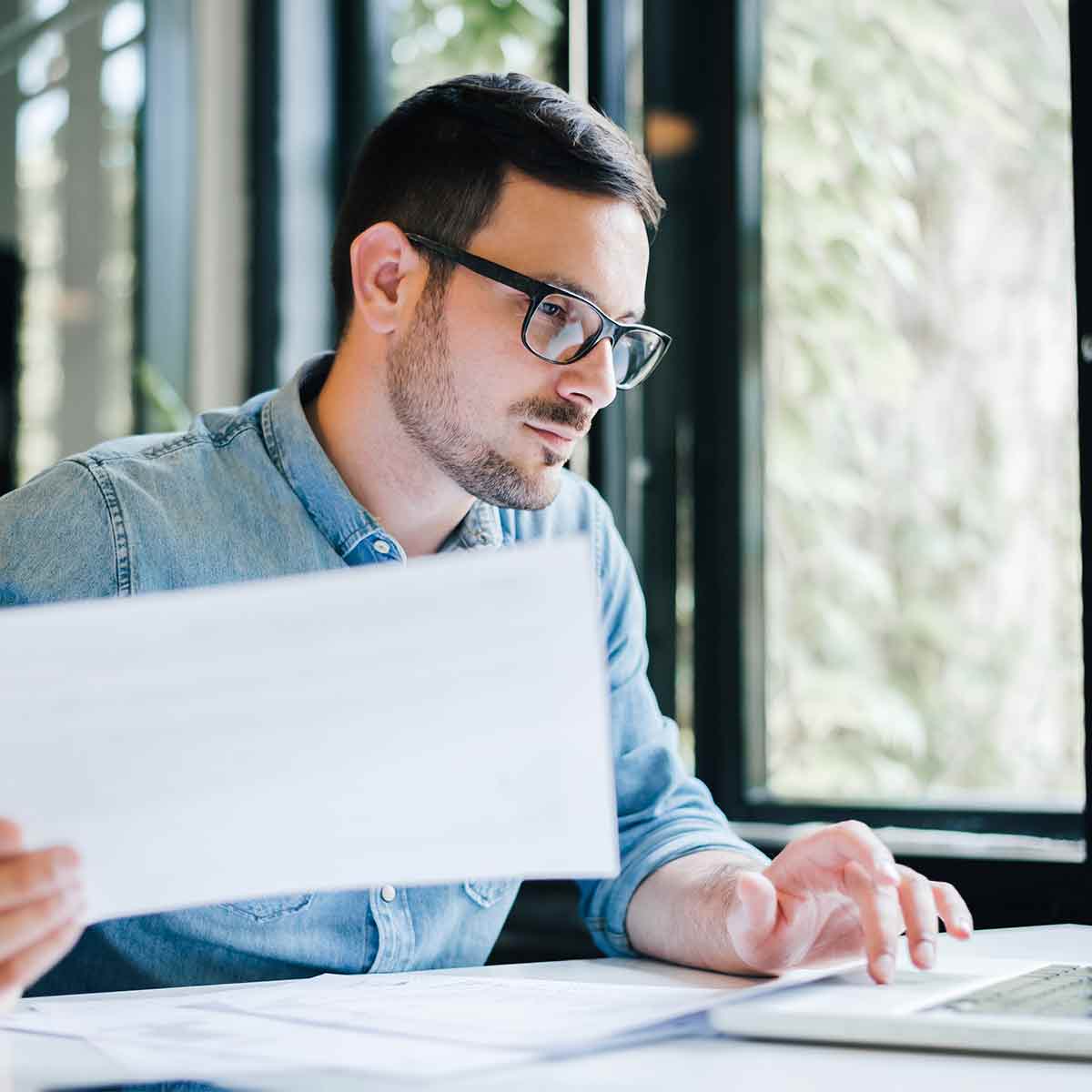 Man reviewing paper financial documents while working on a laptop